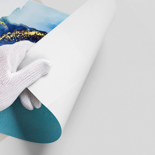 Close-up of hands in white gloves peeling back white backing of abstract deep blue, teal, and gold ink poster material