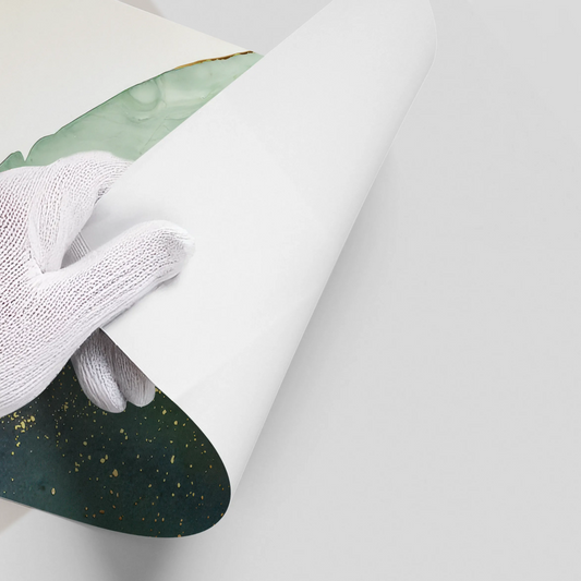 Close-up of hands in white gloves peeling back white backing of abstract dark green and gold ink poster material