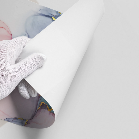 Close-up of hands in white gloves peeling back white backing of abstract blue, pink, and gold ink poster material