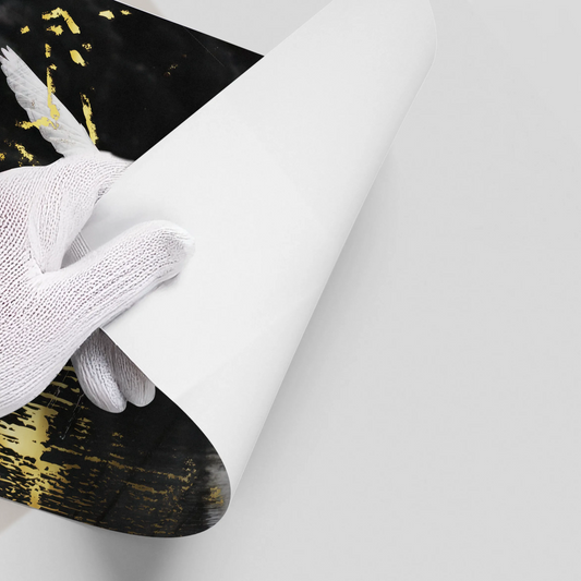 Hand in white glove curling back the corner of the black and gold abstract bird art poster.