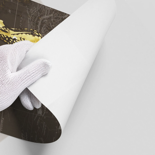 Close-up of a hand in a white glove peeling back the corner of the metallic gold giraffe poster on a dark map background.