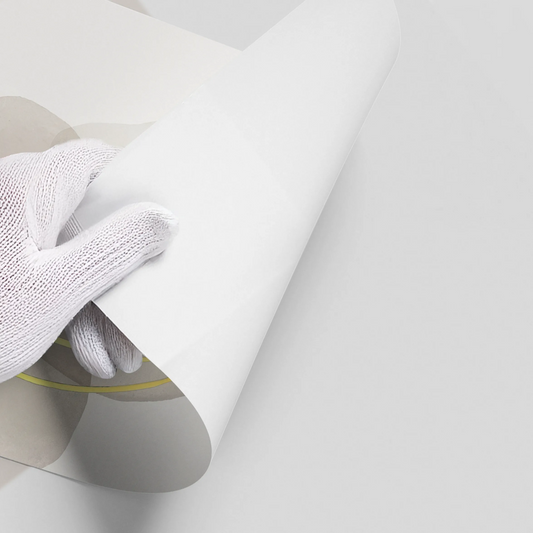 Close-up of hands in white gloves peeling back white backing of abstract minimal beige gray and gold ink poster material