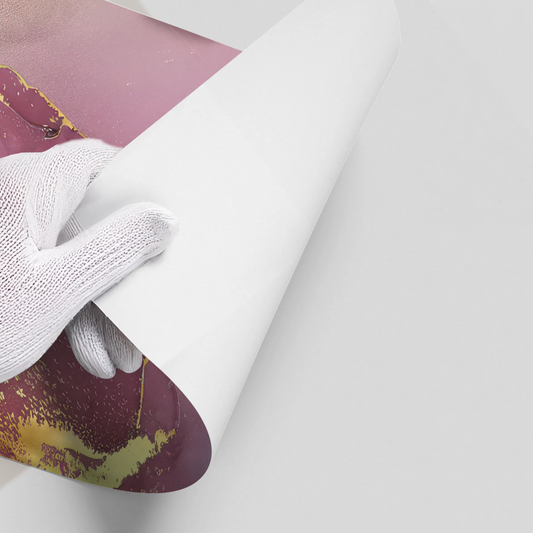 Close-up of hands in white gloves peeling back white backing of abstract pink, purple, gray, and gold ink poster material