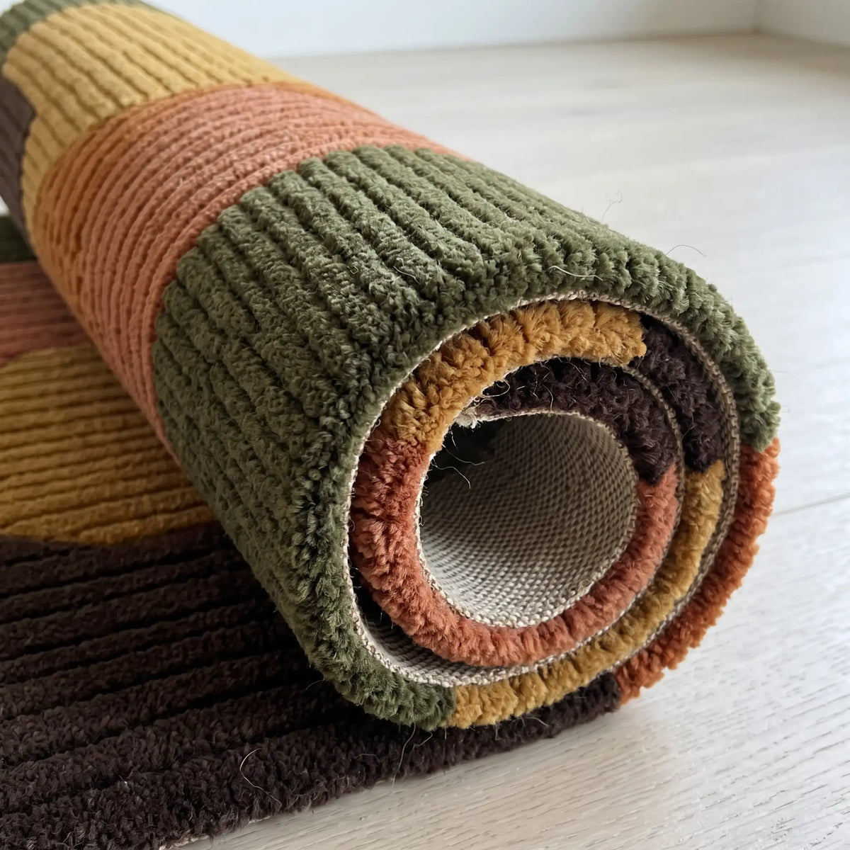 Arcadia modern abstract rug in Olive Terracotta – rolled to show the backing and thickness