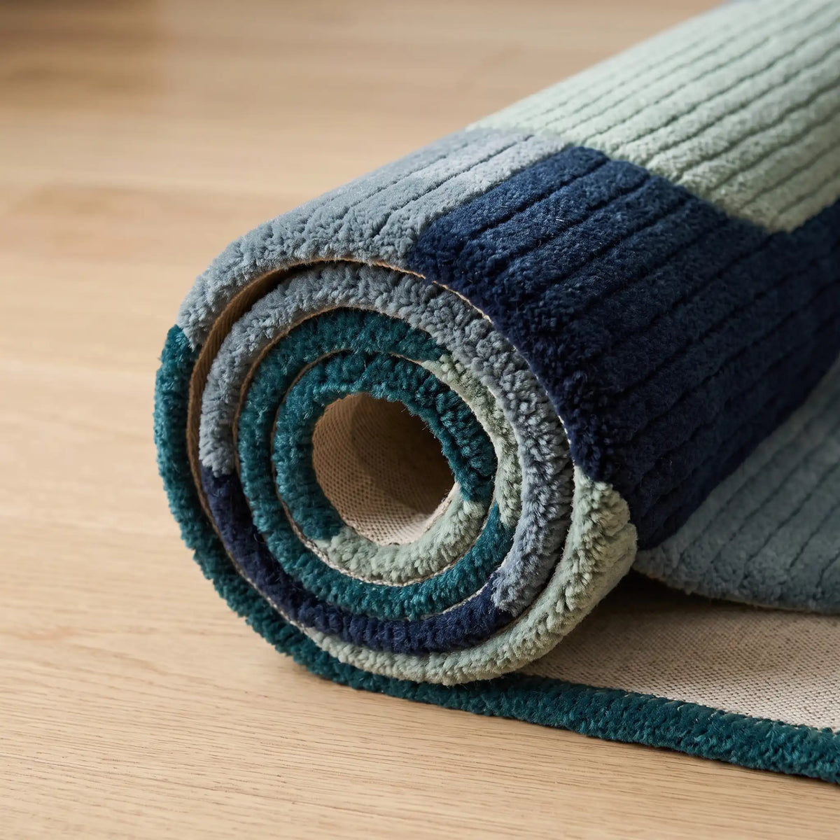 Arcadia modern abstract rug in Teal Slate – rolled to show the backing and thickness