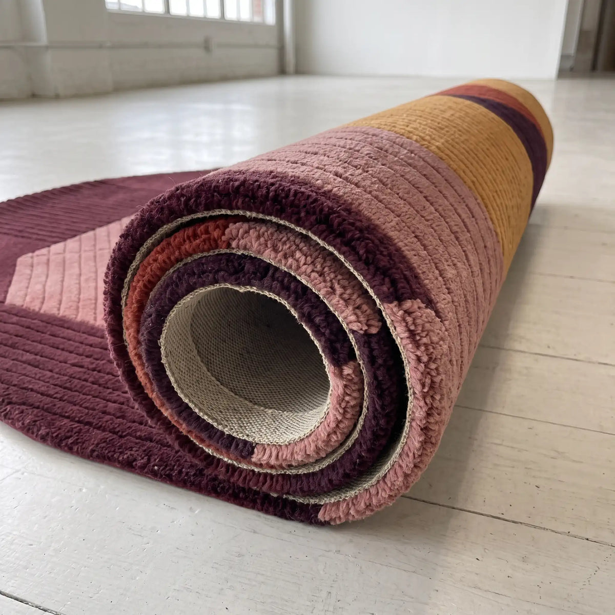 Arcadia modern abstract rug in Burgundy Ochre – rolled to show the backing and thickness