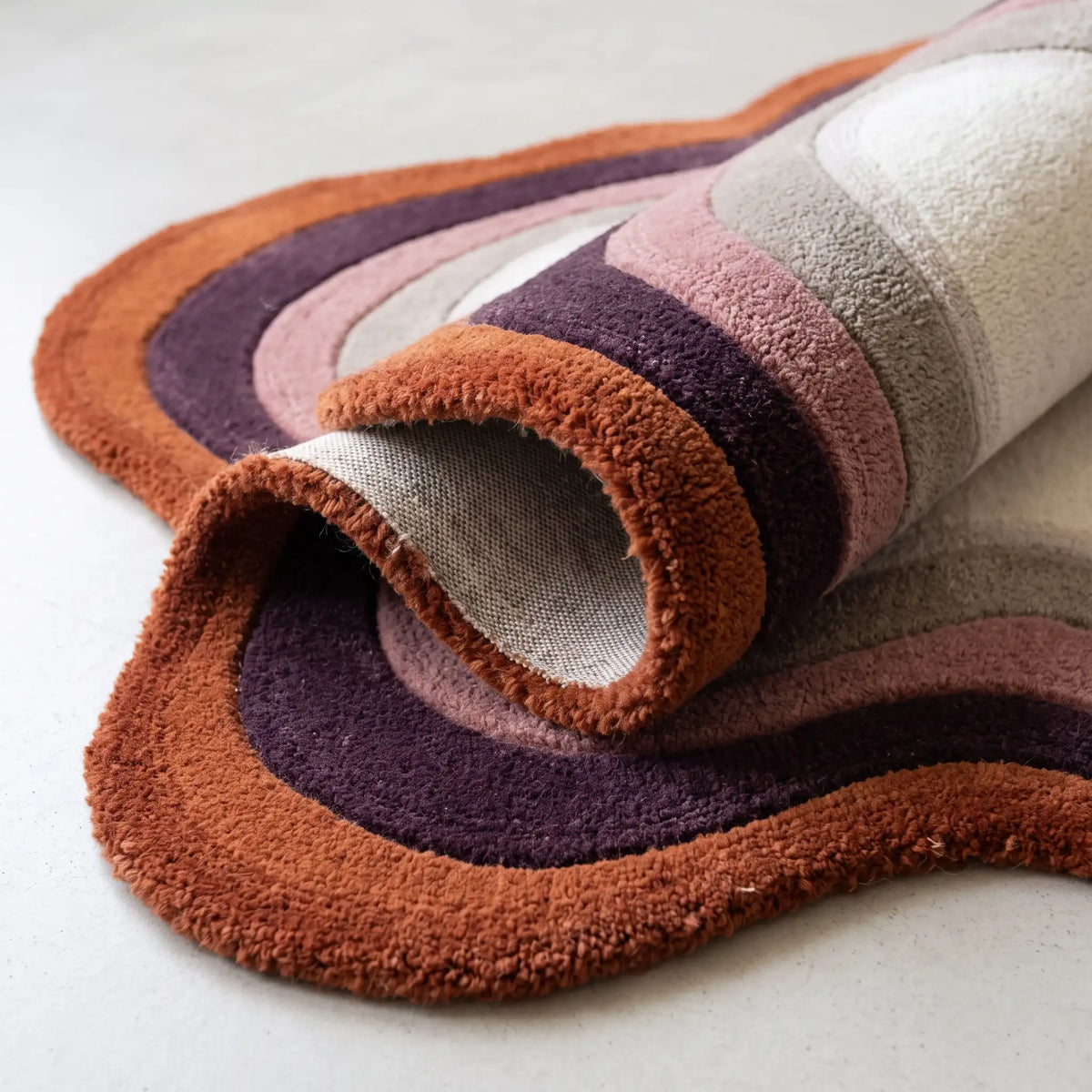 Echo Pool modern abstract rug in Rust Plum – rolled to show the backing and thickness